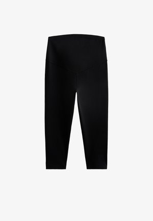 Leggings noirs longueur cheville en tissu extensible, dotés d'une taille haute et large, avec une finition lisse et mate. Sans motifs ni accents.