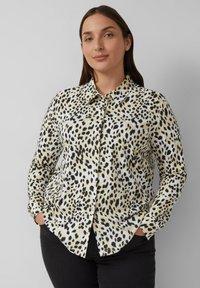 Knoopshirt met een beige achtergrond en een zwart luipaardprintpatroon. Gemaakt van een gladdige stof, heeft het een kraag en lange mouwen.