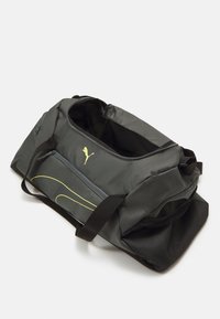 Sivi duffel torba s crnim akcentima, koja ima veliki glavni odjeljak, žuti logo, detalje sa zip zatvaračem i strukturiranu mrežastu stranu.