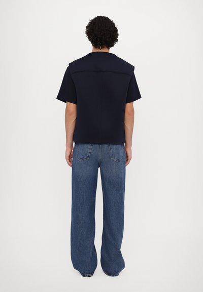 Haut marine à manches courtes avec épaules structurées et coupe cintrée, associé à un jean en denim bleu clair et délavé.