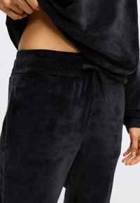 Zwarte velours joggers met een elastische tailleband, verstelbare koorddetail en een zachte textuur; aansluitend rond de heupen met zijzakken.