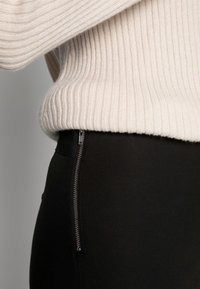 Czarne legginsy z bocznym zamkiem błyskawicznym, zestawione z jasnobeżowym prążkowanym sweterkiem dzianinowym, podkreślającym fakturę i kontrast kolorów.