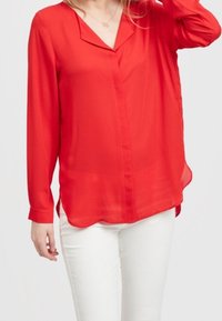 Blusa rossa a maniche lunghe con scollatura a V e chiusura a bottoni. Tessuto leggero e trasparente con una vestibilità comoda; orlo curvo e spacchi laterali.