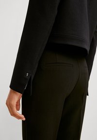 Schwarzer Hoodie mit einem cropped Design und Fischgrätmuster, kombiniert mit maßgeschneiderten schwarzen Hosen, die subtile Gesäßtaschen aufweisen.