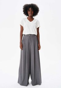 Witte V-hals T-shirt met opgerolde mouwen, gecombineerd met grijze, hoge taille, wijde broek met knoopsluiting en zijzakken.