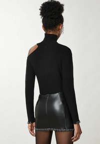 Maglione nero in maglia con texture a coste, colletto alto e design con spalle scoperte, abbinato a una mini gonna in pelle nera con dettagli in metallo.