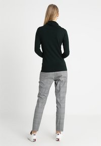 Col roulé vert foncé à manches longues avec une coupe décontractée, associé à un pantalon à carreaux gris clair et des baskets blanches. Design simple et texture douce.