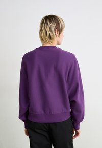 Lilla sweatshirt med lange ærmer, ribbede manchetter og rund hals, med en afslappet pasform og blød tekstur, båret med sorte bukser.