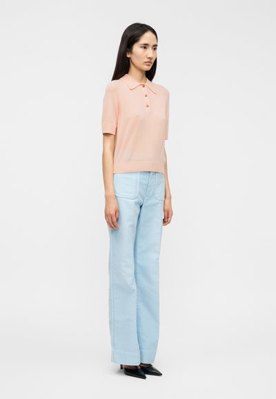 Ανοιχτό ροδακινί κοντομάνικο πόλο με κλασικό γιακά και λεπτομέρεια με  κουμπιά, σε συνδυασμό με ψηλόμεσα, ανοιχτό μπλε παντελόνια φαρδιάς γραμμής και μαύρα μυτερά τακούνια.