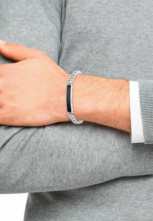 Bracciale in argento con un elegante accento rettangolare nero, indossato su un polso sopra un maglione grigio, che mette in risalto un design moderno e minimalista.