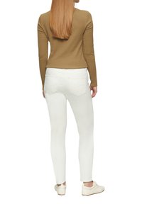 Witte skinny jeans en een aansluitend bruin longsleeve top. De jeans hebben achterzakken en een gladde textuur. De schoenen zijn witte casual sneakers.