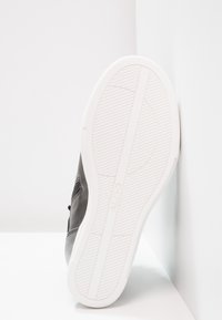 Black sneaker with a smooth leather upper, white rubber sole, and textured details. Features a minimalist design with no visible logos.