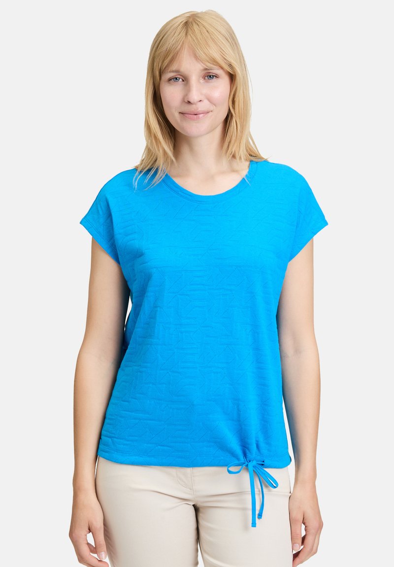 Niebieska bluzka z krótkim rękawem, z teksturowanym wzorem, okrągłym dekoltem i regulowanym dołem ze sznurkiem. Wykonana z lekkiego materiału.