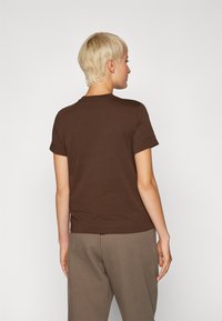 T-shirt in cotone marrone con maniche corte e scollatura rotonda, caratterizzato da una texture liscia e da un design semplice e aderente.