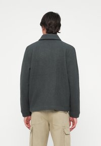 Grå fleecejakke med krage, hele ermer og rett passform, paret med beige cargo-bukser.