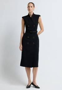 Czarna sukienka bez rękawów z zawiązywanym fasonem, podwójnymi złotymi guzikami oraz szerokim paskiem z kwadratową klamrą. Gładka faktura.