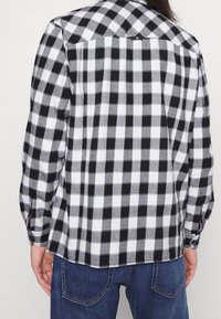 Koszula w kratę w czarno-białe wzory; miękka w dotyku z kołnierzykiem na guziki i długimi rękawami, z rozcięciem u dołu z tyłu.
