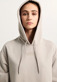 Světle béžová mikina vyrobená z měkkého materiálu s přední klokaní kapsou. Obsahuje kapuci se šňůrkou a vyšívané logo na hrudi.