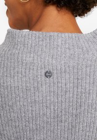 Maglione grigio a maglia con un design a coste testurizzate, con scollatura rotonda e una piccola etichetta nera sul retro.