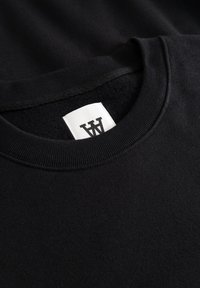 Sweat-shirt noir avec un col côtelé et une étiquette en tissu. Le matériau semble doux avec une texture lisse, mettant en valeur un design simple.