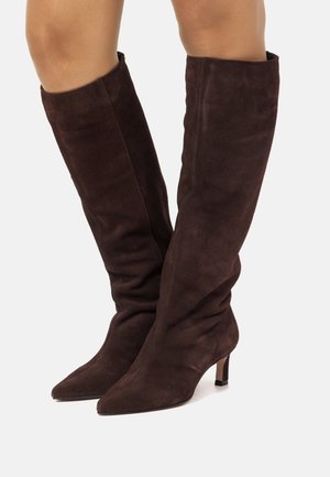 Bottines en daim marron au-dessus du genou avec un bout pointu et un talon fin, conçues avec un ajustement décontracté le long de la jambe.