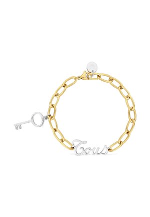 Gold chain bracelet with a silver key charm and a silver script tag reading "Tous" on a white background.