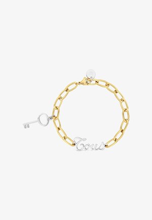 Pulsera de cadena de oro con un colgante de llave de plata y una placa de plata con la inscripción "Tous" sobre un fondo blanco.