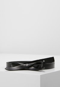 Cinturón de cuero negro con una textura suave y un detalle de lazo, que presenta un agujero para ajustes. Diseño simple y elegante.