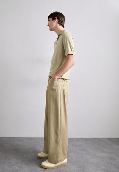Ljusgrön kortärmad polo skjorta kombinerad med lediga beige byxor och krämfärgade sneakers, vilket visar en enkel, modern design.