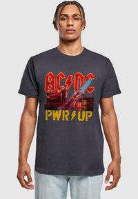 Sort bomulds T-shirt med et levende AC/DC grafisk design, med gult "PWR UP" tekst og et mønster, der viser en live bandoptræden.