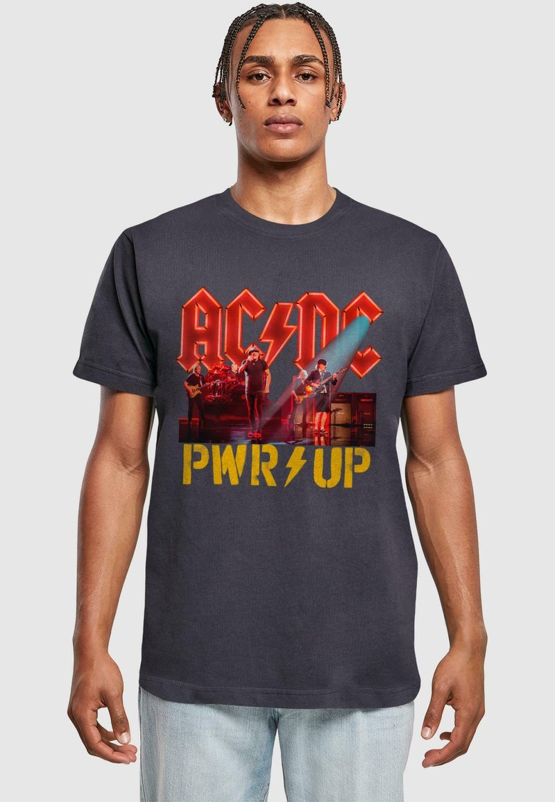 Sort bomulds T-shirt med et levende AC/DC grafisk design, med gult "PWR UP" tekst og et mønster, der viser en live bandoptræden.