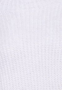 Valkoinen ribbineulottu kangas, jossa pystysuoria viivoja ja pehmeä rakenne, ilman näkyviä kuvioita tai laitteiston yksityiskohtia.