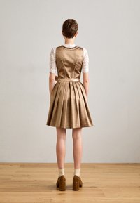 Robe plissée dorée avec un haut en dentelle à manches courtes, mettant en avant un détail de ceinture, portée avec des chaussures à talons épais marron et des chaussettes à motifs.