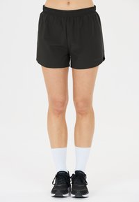 Schwarze sportliche Shorts mit elastischem Bund, glatter Textur und seitlichen Schlitzen für erhöhte Beweglichkeit. Kombiniert mit schwarzen Sneakern und weißen Socken.
