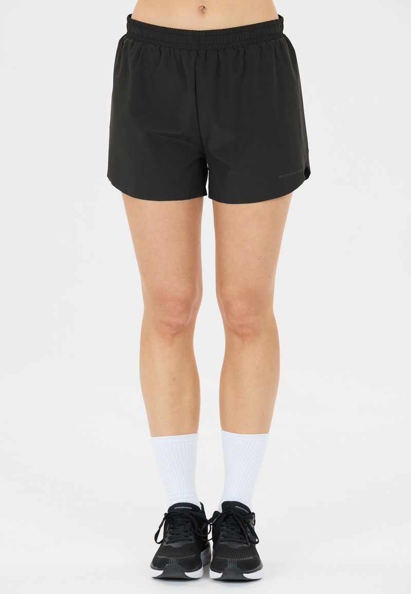 Schwarze sportliche Shorts mit elastischem Bund, glatter Textur und seitlichen Schlitzen für erhöhte Beweglichkeit. Kombiniert mit schwarzen Sneakern und weißen Socken.