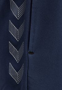 Marinfärgad tyg med en texturerad yta, prydd med vertikala randiga chevronmönster i silver. Inkluderar en svart knappdetalj vid sidosömmen.