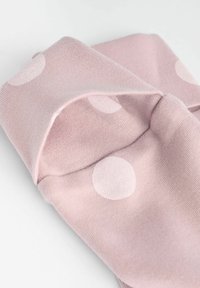 Rózsaszín anyag fehér pöttyökkel, puha tapintású, szépen összehajtogatva. A pöttyök mérete változó, játékos, mégis egyszerű mintát alkotva.