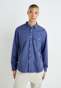 Camisa azul de manga larga, con bolsillo en el pecho y botones blancos. Fabricada con una tela ligera y de textura suave.