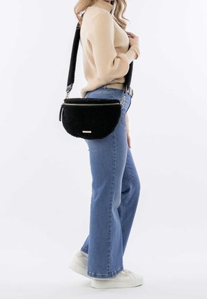 Sacoche en sherpa noir avec une forme incurvée, matériel doré et fermeture éclair. Associée à un jean évasé bleu clair et un pull beige.