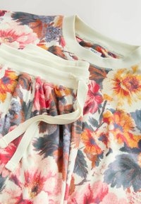 Felpa e pantaloni jogger con motivo floreale in tessuto morbido. Presenta tonalità vivaci di rosso, giallo e blu con dettagli beige e stringa di regolazione.