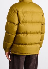 Olivengrøn polstret jakke med vandret quiltning, høj krave og ribstrikkede manchetter. Inkluderer snøre i kanten for justerbar pasform.