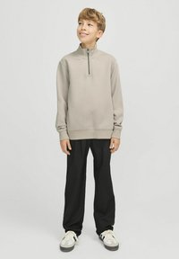 Ljusgrå halvzip-tröja, mjukt material, avslappnad passform. Kombinerad med svarta lösa byxor och grå sneakers med vita detaljer.