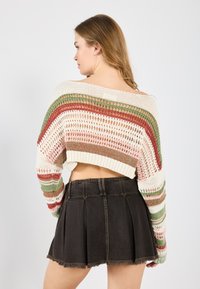 Häkelpullover mit mehrfarbigen Streifen in Creme, Grün, Rot und Pink, kombiniert mit einem schwarzen Denim-Minirock mit Falten.