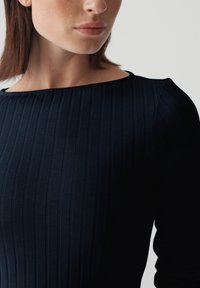 Marineblaues Rippkleid mit Bootsausschnitt und langen Ärmeln, aus einem strukturierten Stoff, der die figurbetonte Silhouette betont.