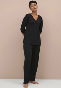 Zwart pyjama set met een V-hals top met kantdetails en driekwart mouwen, gecombineerd met bijpassende loszittende broeken. Zachte stof.