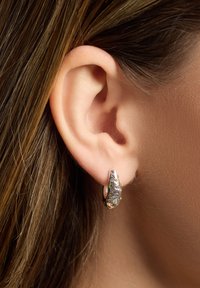 Silberohrstecker mit strukturiertem Design, verziert mit kleinen rosa und grünen Edelsteinen, getragen am Ohrläppchen eines menschlichen Ohrs.