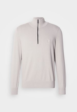 Light beige pullover with a high collar, featuring a half-zip front. Knit fabric with ribbed cuffs and a small logo patch on the chest.