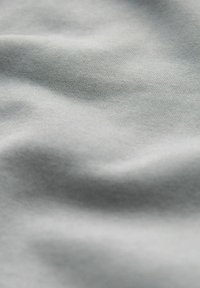 Tejido gris claro con una textura suave y lisa, que presenta ondulaciones sutiles y un patrón de punto fino. Material ligero y flexible.