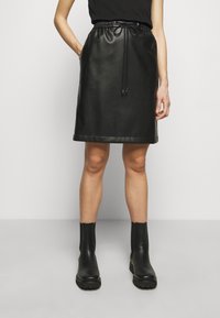 Schwarze Lederrock mit Kordelzugbund, glatter Textur, A-Linien-Form und einem Saum mit leichtem Glanz, kombiniert mit schwarzen Knöchelstiefeln.