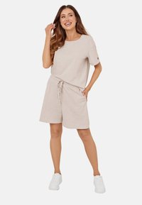 Beżowa bawełniana koszulka z krótkim rękawem i dopasowane szorty z troczkiem. Model nosi białe trampki, prezentując swobodny, codzienny strój.
